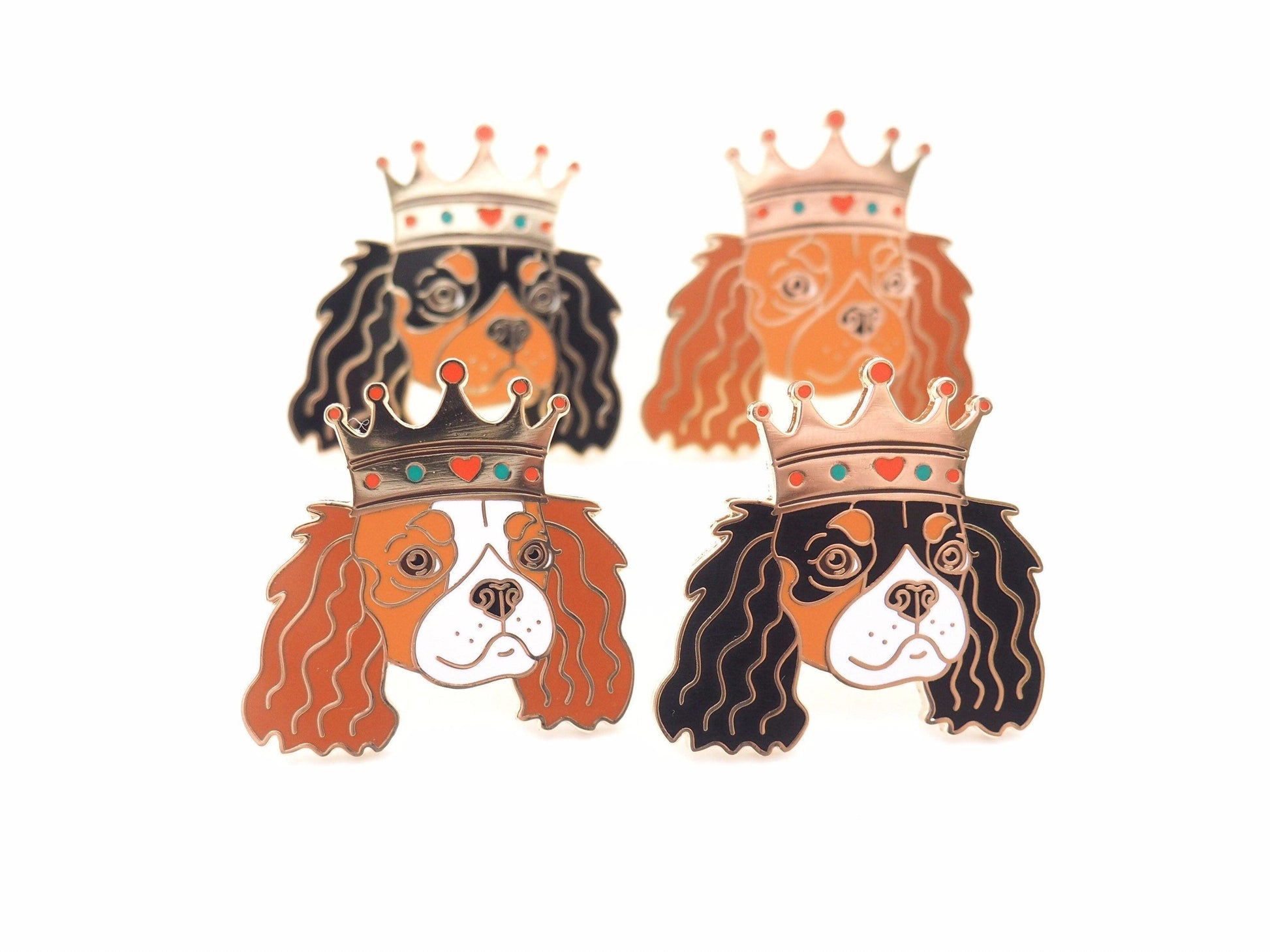 A photo of 4 Cavalier King Charles Spaniel enamel pins, each in a different colour - Blenheim, tri-colour, Black and Tan and Ruby
