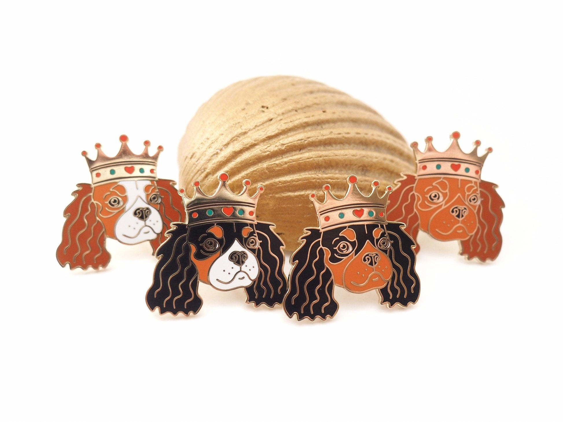 A photo of 4 Cavalier King Charles Spaniel enamel pins, each in a different colour - Blenheim, tri-colour, Black and Tan and Ruby