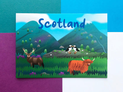A photo of a Scotland themed postcard with mountains, highland cows a stag and 2 puffins