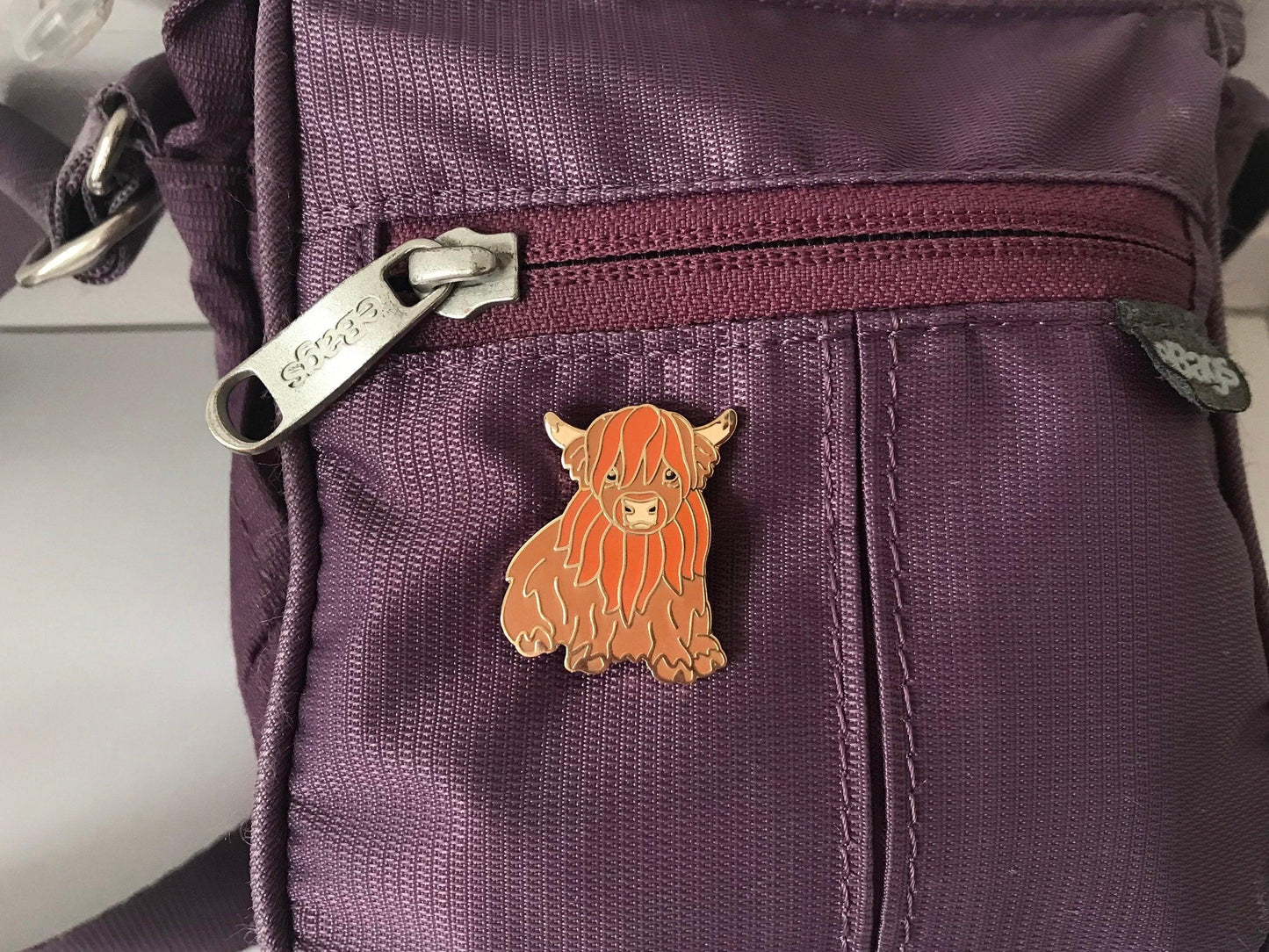 Cute Highland Cow Enamel Pin in a Sitting Position on a purple bag