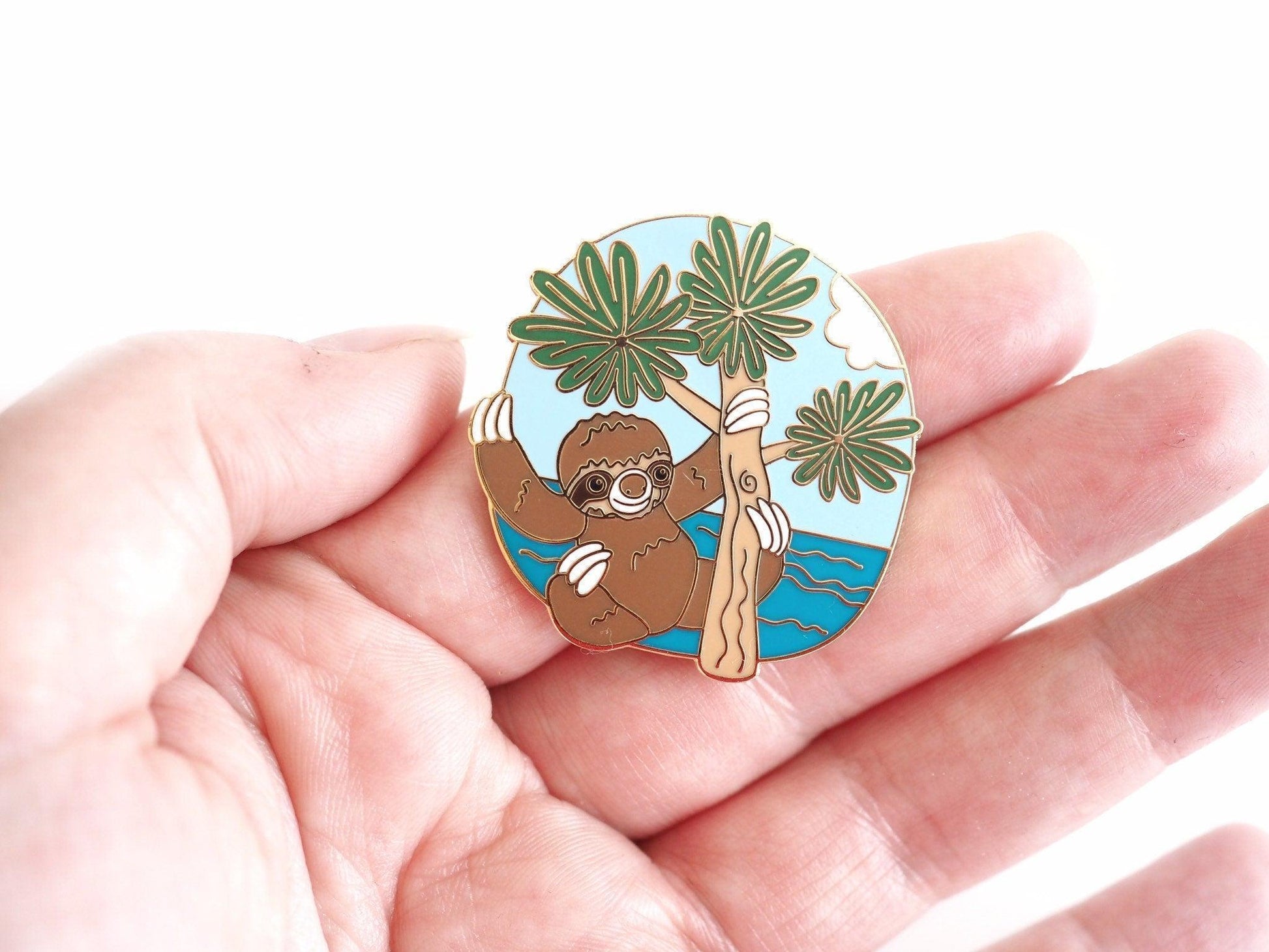 A photo of a sloth enamel pin held in a hand