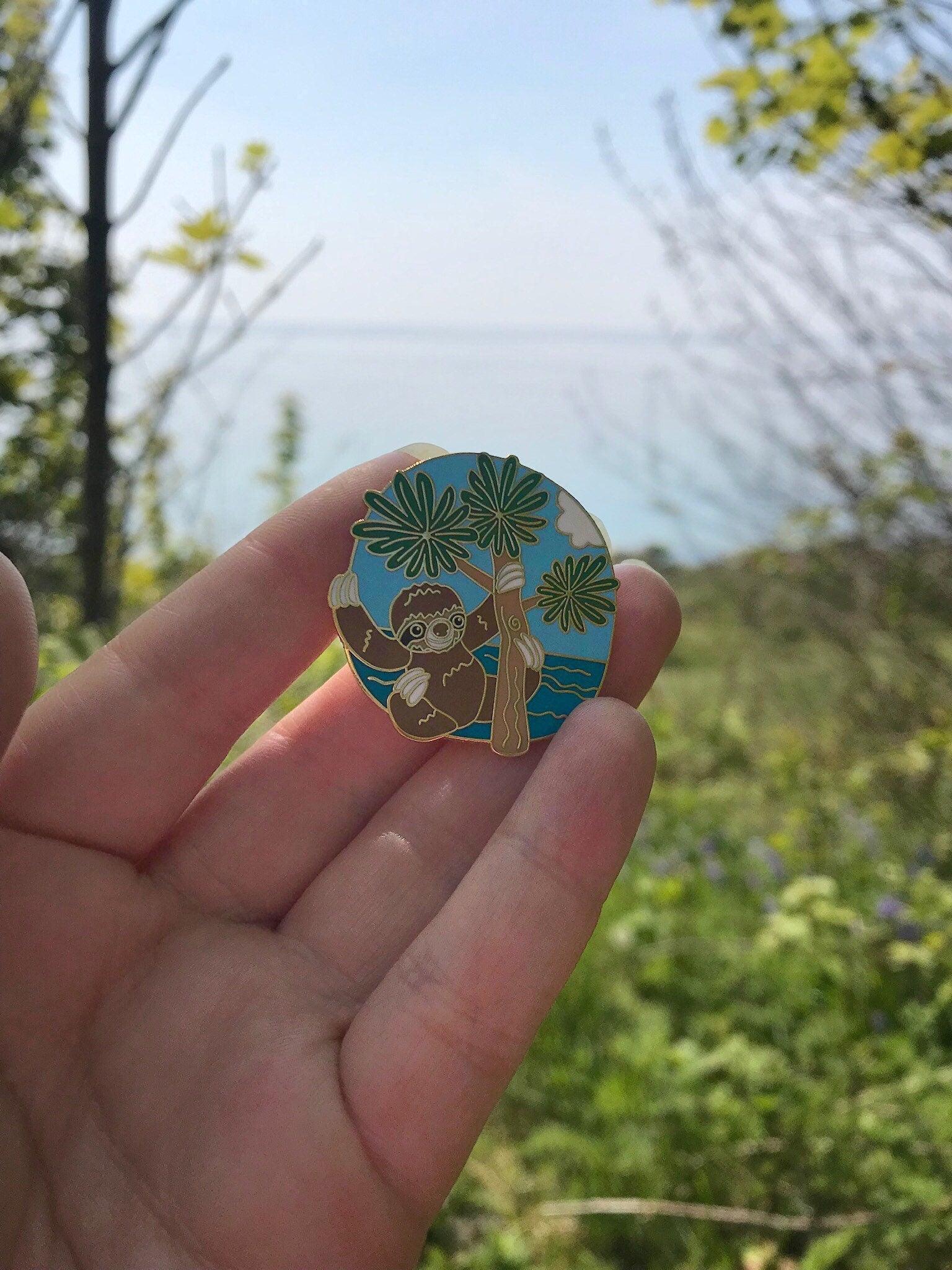 A photo of a sloth enamel pin taken outside