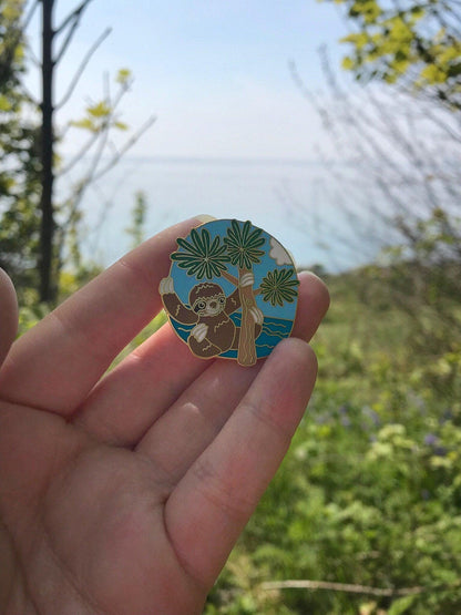 A photo of a sloth enamel pin taken outside